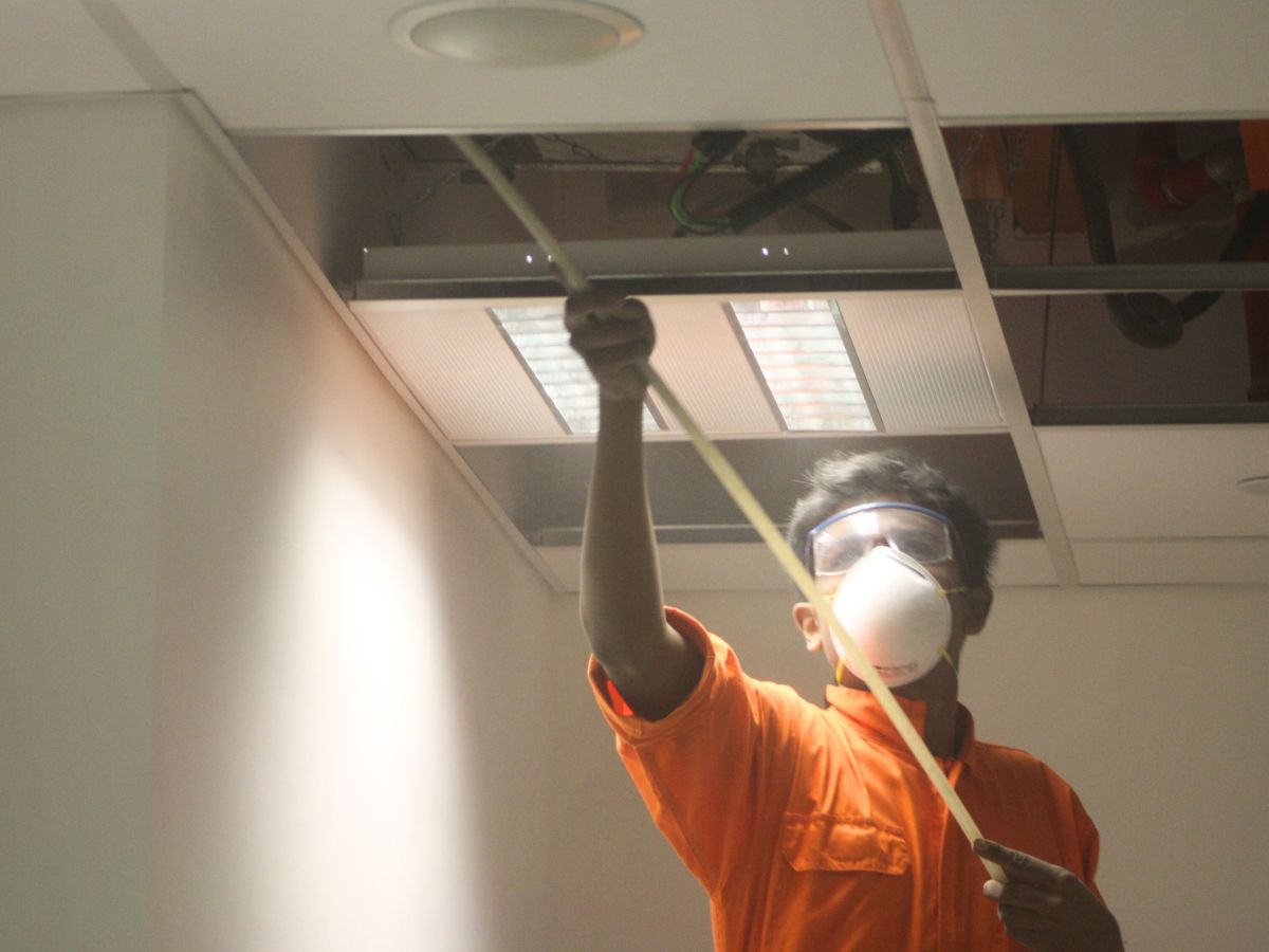 big red personnel cleaning acmv duct in an office